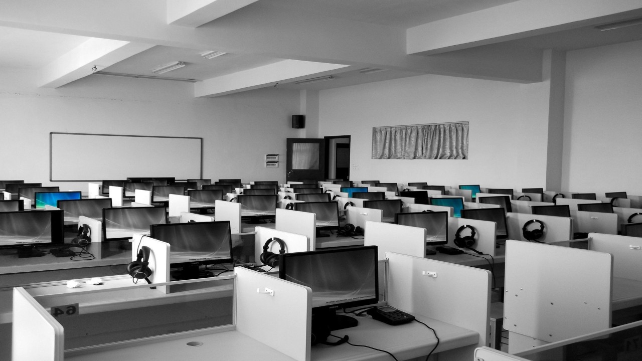 Black and white image of classroom full of work stations with desktop computers.