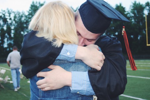 Son wearing graduation rob and cap hugging mother.